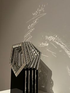 a sculpture is shown in front of a wall with shadows on the wall behind it