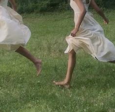 two women in white dresses are playing with a frisbee on the grass outside