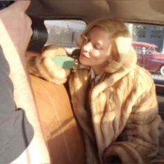 a woman sitting in the back seat of a car wearing a fur coat and holding a cup