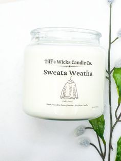 a candle that is sitting on a table next to some flowers and leaves with the words swift's wricks candle co, sweattaweat weatha written on it