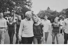 a black and white photo of people walking down the street with their arms around each other