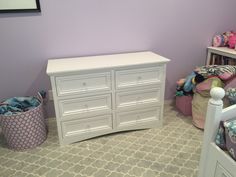 a white dresser sitting next to a purple wall in a child's room with toys