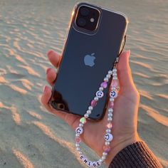 a person holding an iphone in their hand on the beach at sunset with beaded bracelets