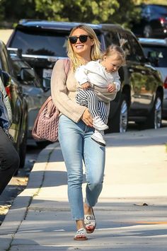 a woman holding a baby walking down the street