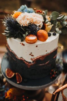 a close up of a cake with flowers and fruit on the top, sitting on a table