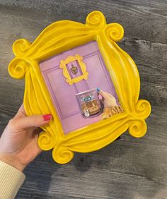 a person holding up a yellow frame with pictures in it on top of a wooden table