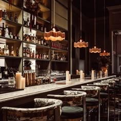 an empty bar with stools and bottles on the shelves in front of it is lit by candles