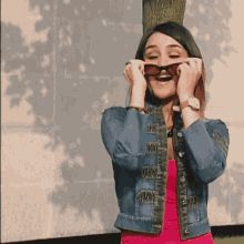 a woman in a pink dress and jean jacket is holding her glasses up to her face