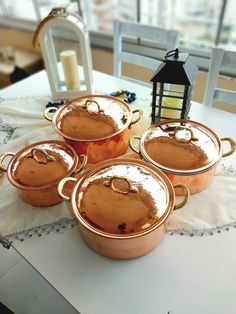 four copper pots sitting on top of a table next to a lantern and window sill