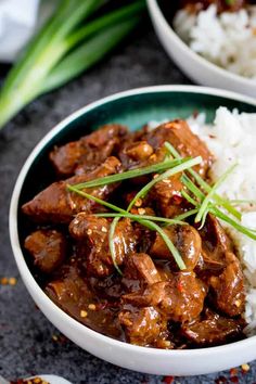 a white bowl filled with meat and rice on top of a black table next to chopsticks