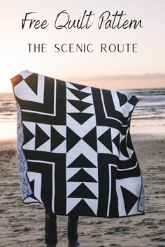 a person standing on top of a sandy beach holding a black and white geometric quilt