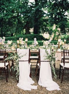 an outdoor table set up with white linens and greenery