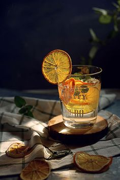 an orange drink is garnished with sliced oranges on a wooden board and plaid tablecloth