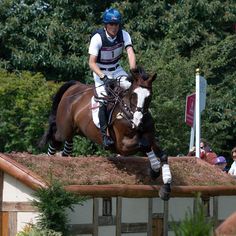 a man riding on the back of a brown and white horse over an obstacle course