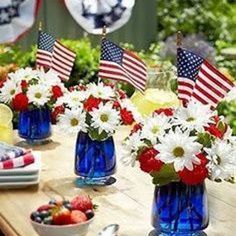 red, white and blue flowers are in vases on a table with american flags