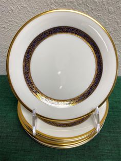 two white plates with gold trim on each one and green table cloth under them,