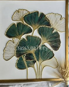 an art work with gold and green leaves on white paper, framed in a golden frame