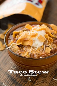 a bowl of chili and tortilla soup with sour cream on top, sitting on a wooden table