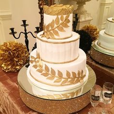 a three tiered white and gold wedding cake on a table with two wine glasses