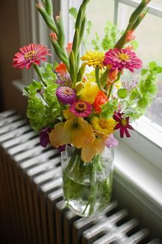 a vase filled with lots of colorful flowers on top of a radiator next to a window