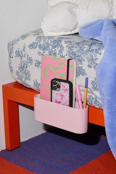 there is a pink holder with pens, notebooks and cell phones in it on the bed