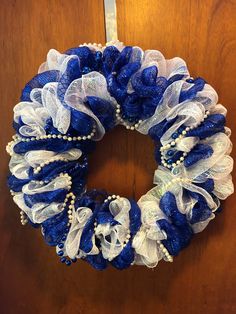 a blue and white wreath hanging on the front door with pearls, beads and mesh