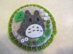 a felt brooch with a hippo face and green leaves on the front, sitting on a white surface