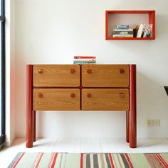 a wooden dresser sitting in front of a window next to a striped rug and bookshelf