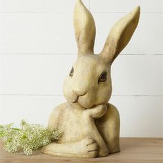 a statue of a rabbit sitting on top of a wooden table next to a plant