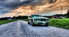 a green mustang car parked on the side of a road in front of a cloudy sky