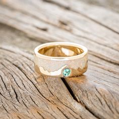 a gold ring with a green stone in the center on a wooden surface, resting on top of a piece of wood