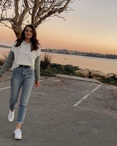 a woman walking across a parking lot next to a tree