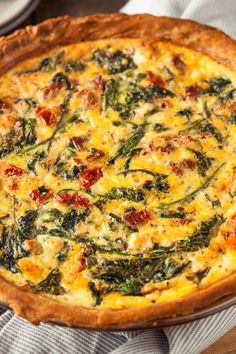 a quiche with spinach and tomatoes on it is sitting on a wooden table