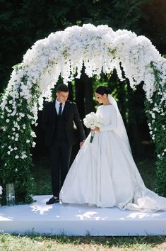 the bride and groom are walking down the aisle under an arch with white flowers on it