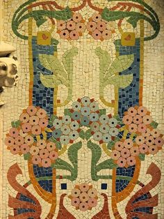 a dog is standing next to a mosaic tile wall with flowers and leaves on it