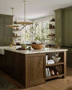 a kitchen with green cabinets and white counter tops, an island in the middle is filled with dishes