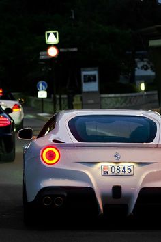 the rear end of a white sports car driving down a street at night with other cars behind it