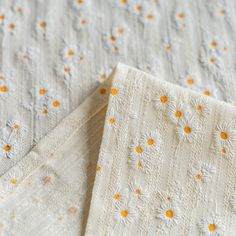 two white bedspreads with yellow and white daisies are laying on top of each other