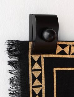 a close up of a black object on a white wall near a rug with fringes