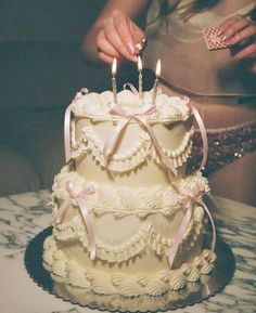 a woman lighting candles on top of a white cake with ruffles and bows