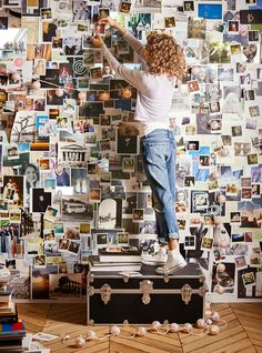 a woman standing on top of a suitcase in front of a wall covered with pictures