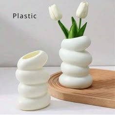 two white vases with flowers in them sitting on a wooden tray next to each other