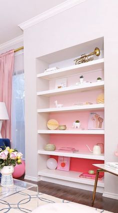 a living room filled with furniture and lots of pink accents on the walls, along with shelves