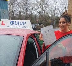 a woman standing next to a red car holding up a blue sign