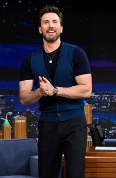 a man standing in front of a tv screen with his hands together and smiling at the camera