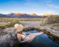 a woman is sitting in the hot springs with mountains in the backgrouund