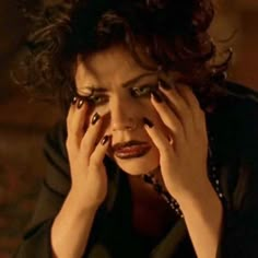 a woman with dark makeup holding her hands to her face and looking at the camera