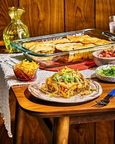 a wooden table topped with plates and bowls filled with food next to a casserole dish