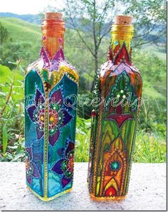 two colorful glass bottles sitting on top of a cement slab in front of some trees