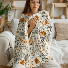 a woman is sitting on the floor wrapped in a white blanket with orange flowers and leaves